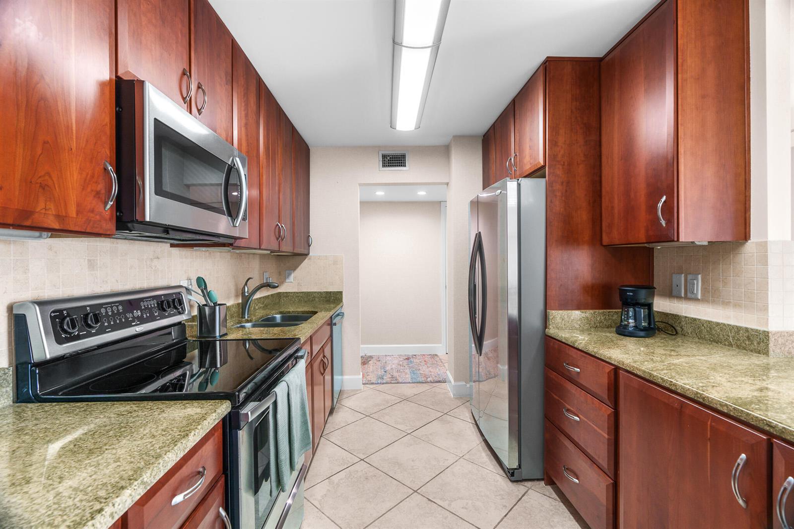 A galley kitchen features cherry wood cabinets, stainless steel appliances, and green granite countertops — 950 Ponce De Leon Road # 4030, Boca Raton FL 33432, BOCA RATON, FL