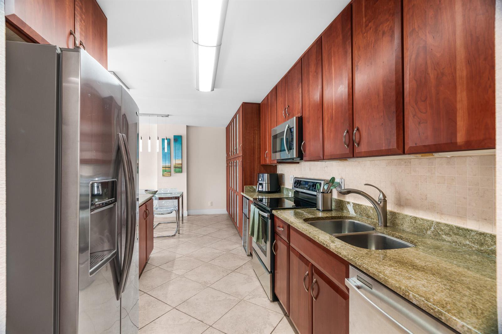A galley kitchen features cherry wood cabinets, granite countertops, and stainless steel appliances — 950 Ponce De Leon Road # 4030, Boca Raton FL 33432, BOCA RATON, FL