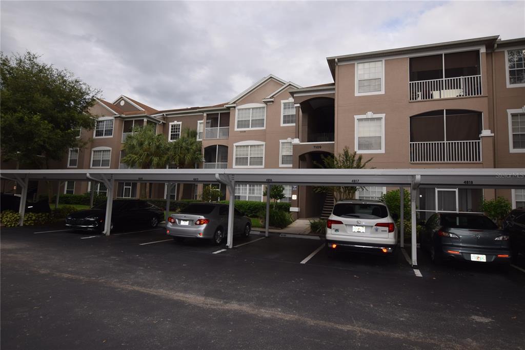 A multi-story apartment building with a covered parking area and several parked cars — 7109 YACHT BASIN AVENUE UNIT 436, ORLANDO, FL