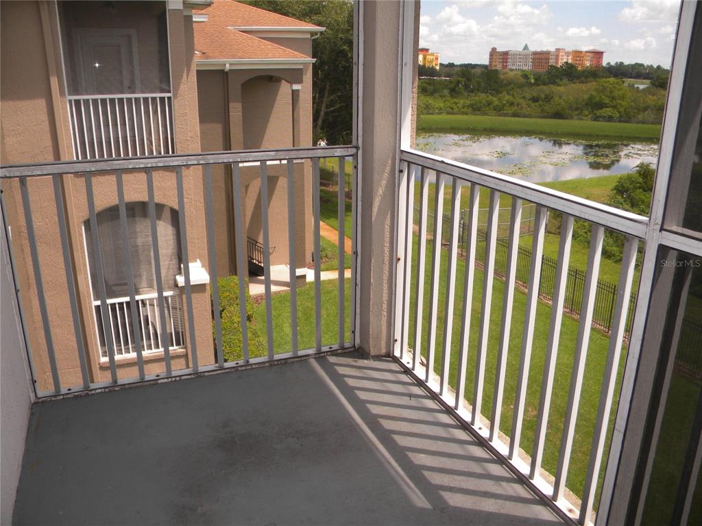 A screened-in balcony overlooks a grassy lawn, a small pond, and a distant building — 7109 YACHT BASIN AVENUE UNIT 436, ORLANDO, FL