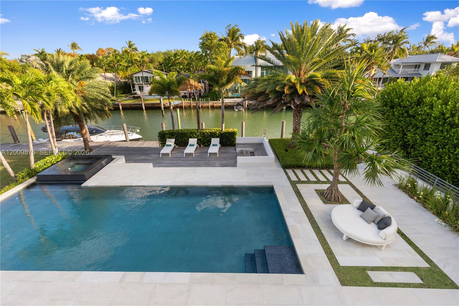 An outdoor pool area features a patio, lounge chairs, a circular daybed, and waterfront views — 120 Knollwood Dr, Key Biscayne FL 33149, KEY BISCAYNE, FL