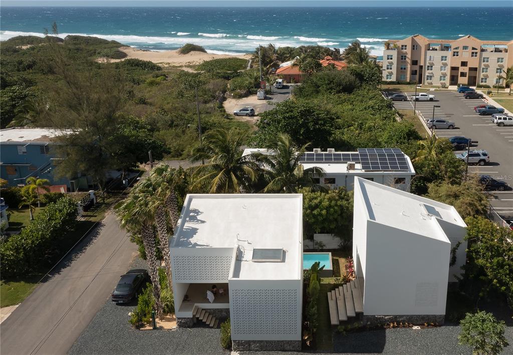 An aerial view shows two modern white buildings with flat roofs near a beach — CASA BAJURA CALLE MONTE DE OCA #7, ISABELA, PR