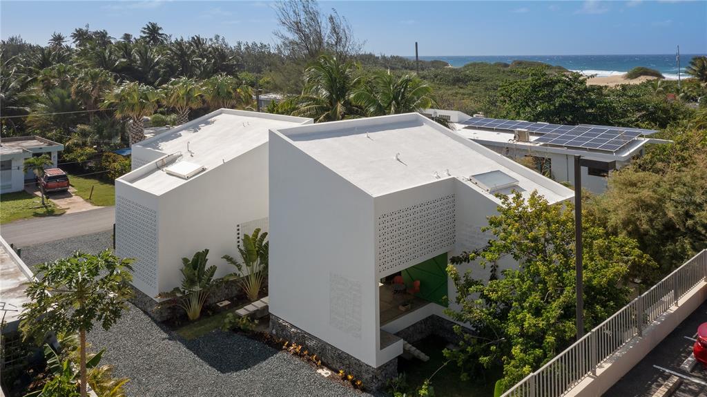 An aerial view shows two modern white houses with slanted roofs near a beach — CASA BAJURA CALLE MONTE DE OCA #7, ISABELA, PR