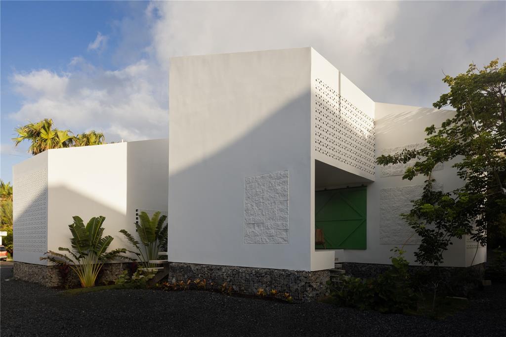 A modern white house with geometric walls, stone foundations, and a green sliding door — CASA BAJURA CALLE MONTE DE OCA #7, ISABELA, PR