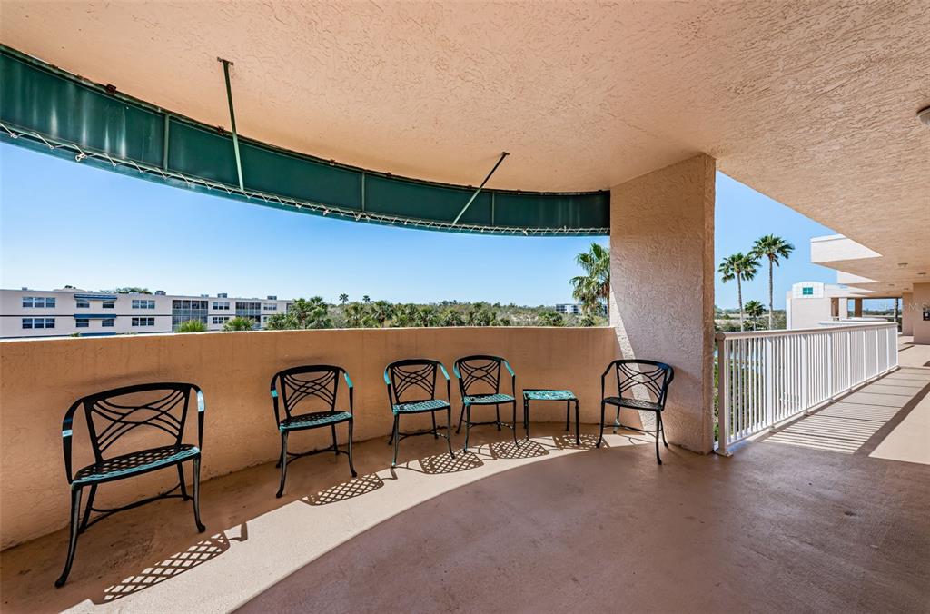 A spacious covered balcony features a curved wall, metal patio furniture, and a scenic outdoor view — 6315 SHORELINE DRIVE UNIT 3307, SEMINOLE, FL