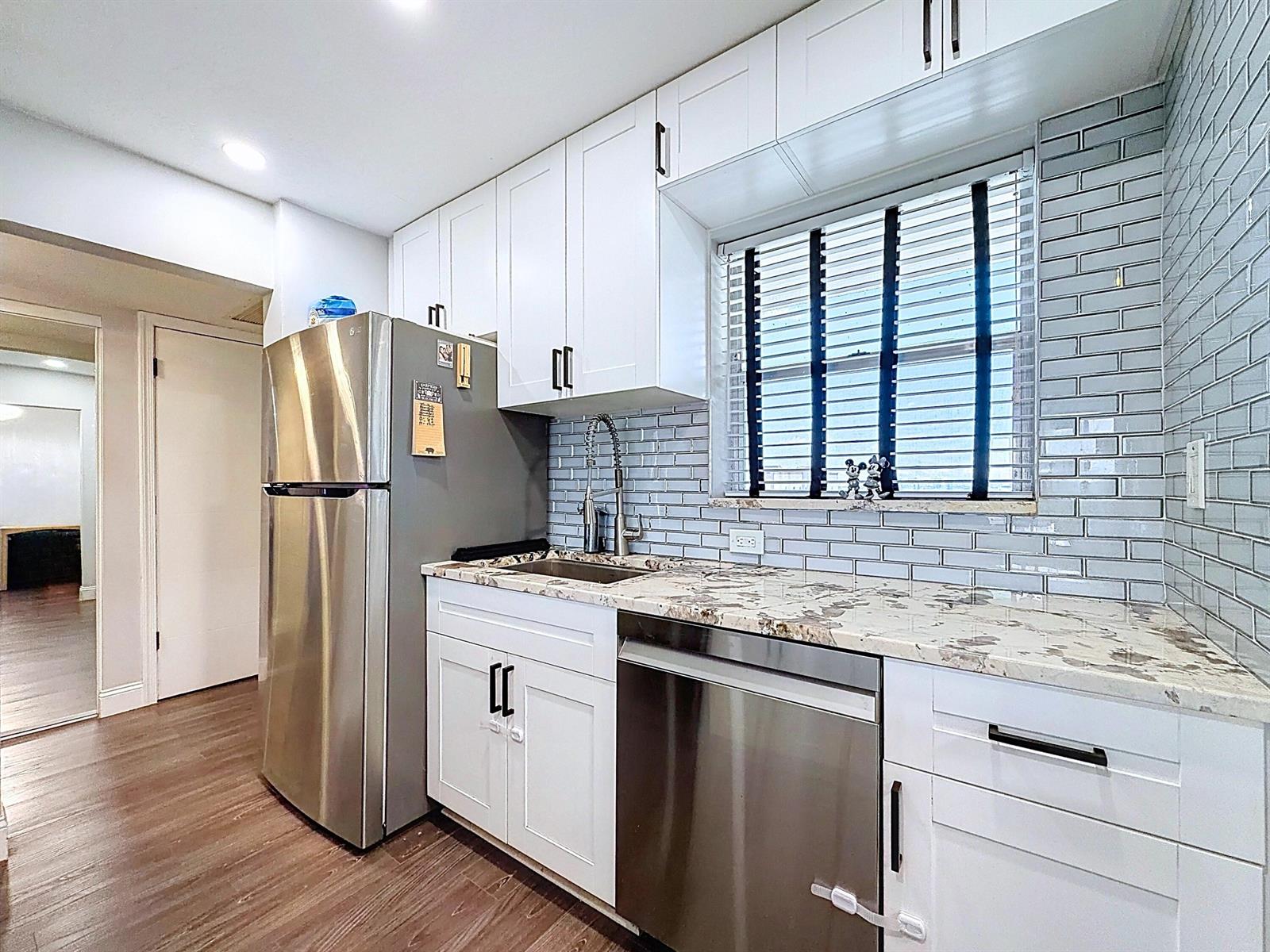 A kitchen features white cabinets, stainless steel appliances, a marble countertop, and gray subway tile — 801 S Federal Highway # 816, Pompano Beach FL 33062, POMPANO BEACH, FL