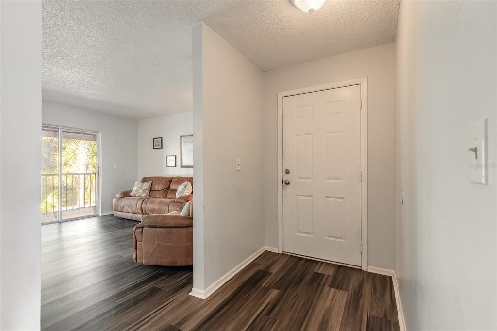 An entryway with wood-look flooring leads into a living room featuring a brown sofa — 426 BANANA CAY DRIVE UNIT I, SOUTH DAYTONA, FL