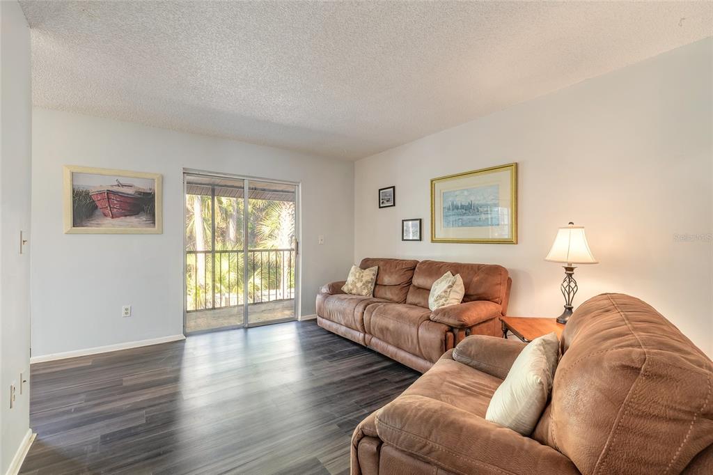 A living room features dark wood-look flooring, two brown sofas, and a sliding glass door — 426 BANANA CAY DRIVE UNIT I, SOUTH DAYTONA, FL