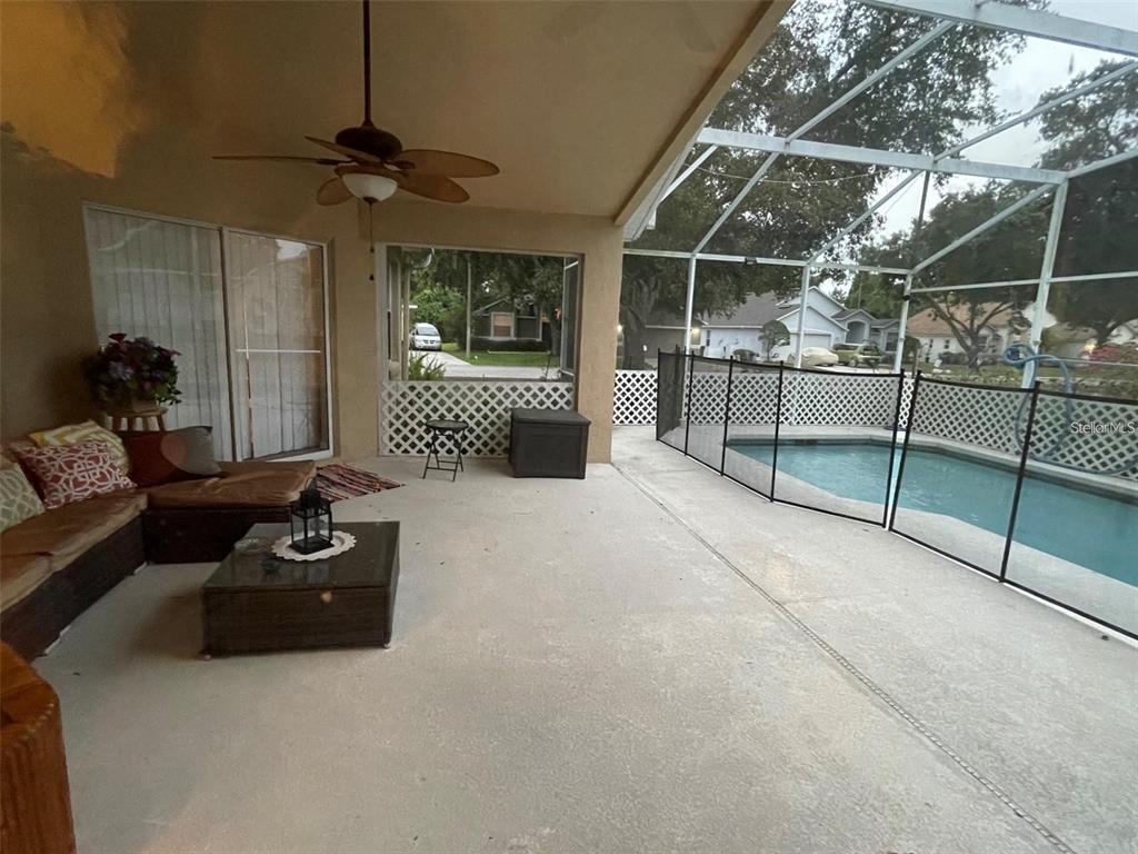A covered patio features a seating area, a ceiling fan, and a screened-in swimming pool — 519 THOUSAND OAKS BOULEVARD, DAVENPORT, FL
