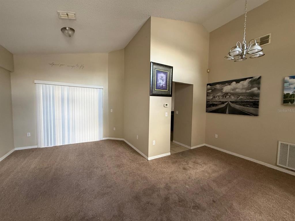 A carpeted dining area features a vaulted ceiling, a chandelier, and a sliding glass door — 519 THOUSAND OAKS BOULEVARD, DAVENPORT, FL