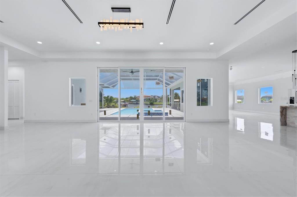 A bright, minimalist living room features white tile floors, a modern chandelier, and sliding glass doors — 9232 ARRID CIRCLE, PORT CHARLOTTE, FL