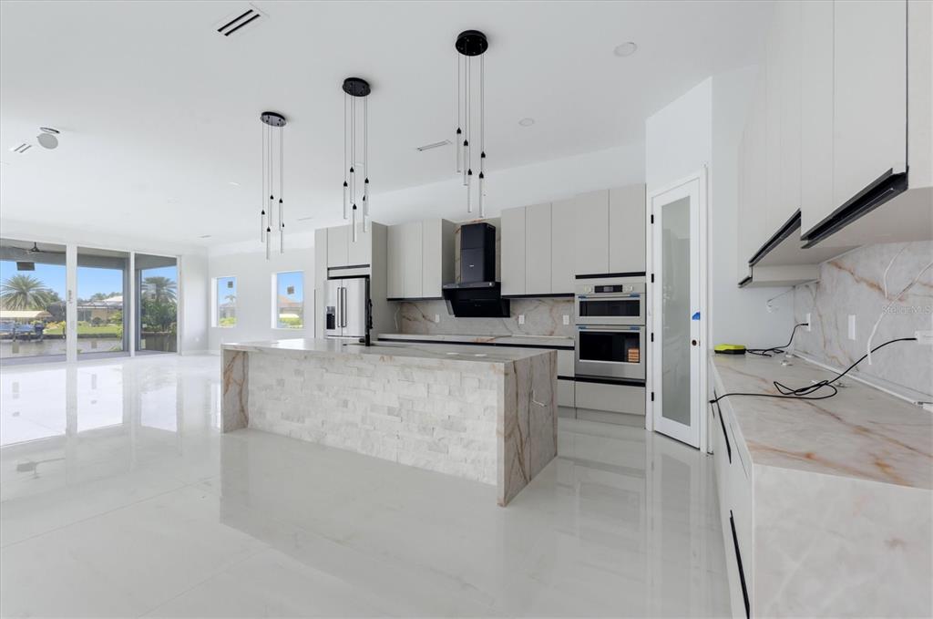 A modern kitchen features a stone-clad island, light cabinetry, and large windows overlooking a canal — 9232 ARRID CIRCLE, PORT CHARLOTTE, FL
