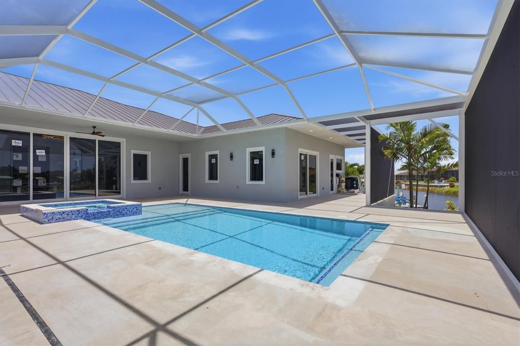 A screened-in patio features a swimming pool, a raised spa, and light-colored stone decking — 9232 ARRID CIRCLE, PORT CHARLOTTE, FL