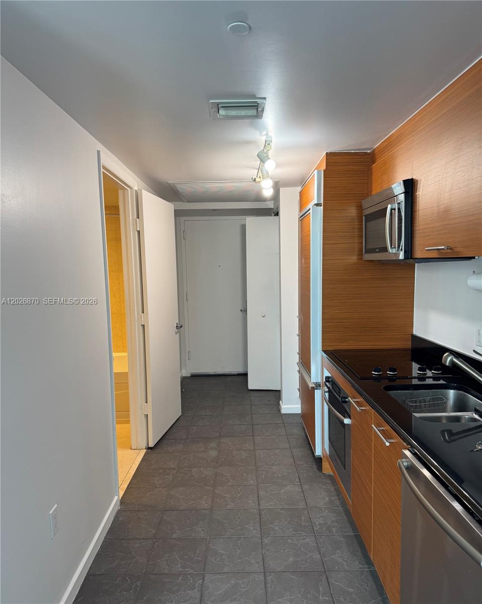 A galley kitchen features wood-grain cabinets, stainless steel appliances, and dark tile flooring — 50 Biscayne Blvd # 3303, Miami FL 33132, MIAMI, FL