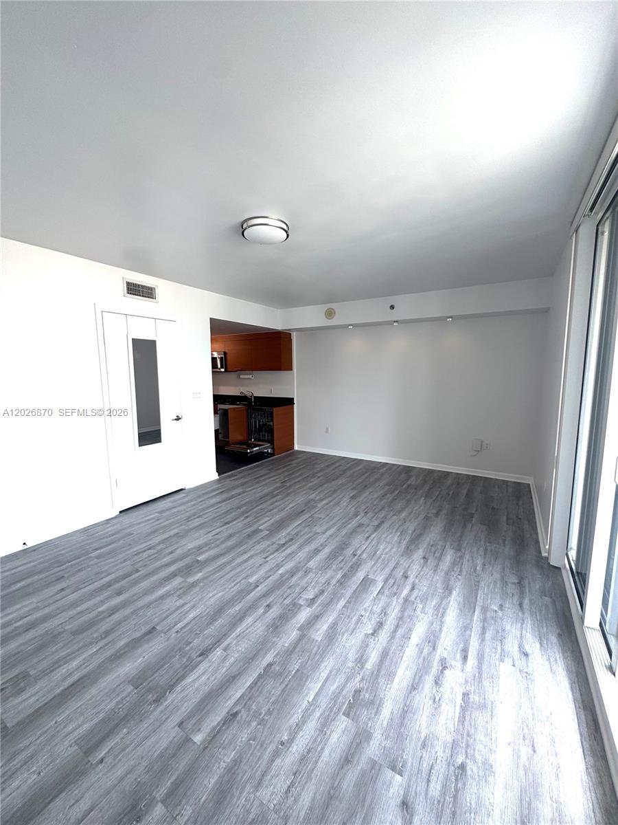 An empty living room features gray wood-look flooring, white walls, and an adjacent open kitchen — 50 Biscayne Blvd # 3303, Miami FL 33132, MIAMI, FL