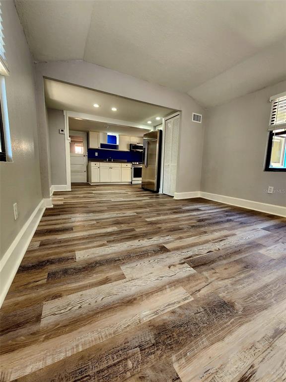 A room with wood-look flooring leads into a kitchen featuring white cabinets and stainless appliances — 2801 18TH STREET N, ST PETERSBURG, FL