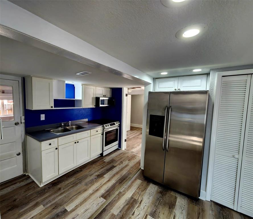 A kitchen features white cabinets, a stainless steel refrigerator, blue walls, and wood-look flooring — 2801 18TH STREET N, ST PETERSBURG, FL