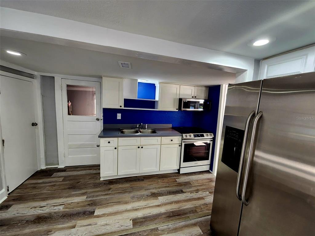 A kitchen features white cabinets, a blue backsplash, stainless steel appliances, and wood-look flooring — 2801 18TH STREET N, ST PETERSBURG, FL