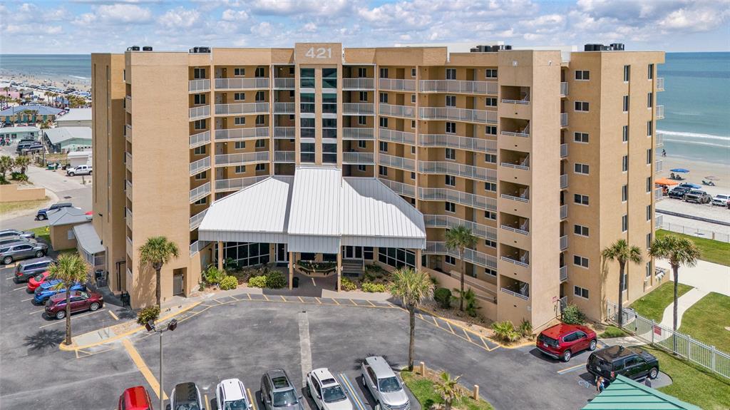 An aerial view shows a multi-story tan apartment building with balconies facing the ocean — 421 S ATLANTIC AVENUE UNIT 302, NEW SMYRNA BEACH, FL