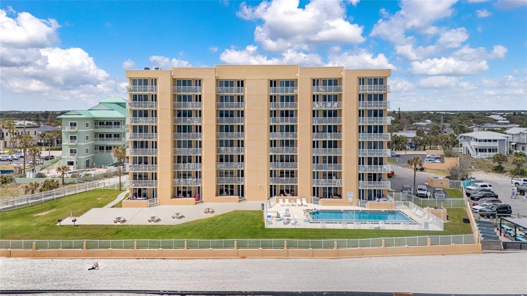 An aerial view shows a multi-story tan apartment building with a pool and beach access — 421 S ATLANTIC AVENUE UNIT 302, NEW SMYRNA BEACH, FL