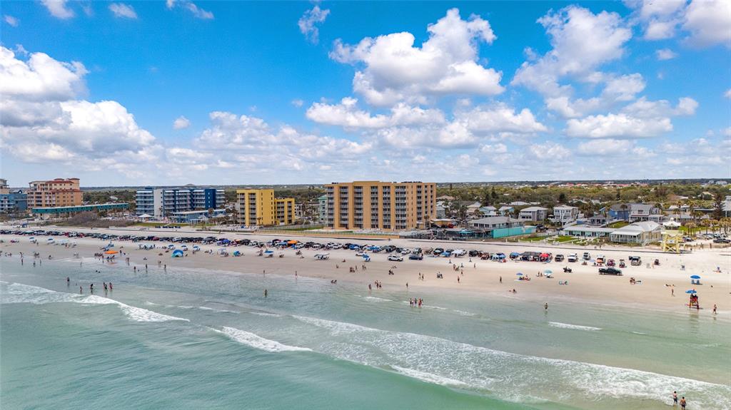 An aerial view of a sandy beach with parked cars, ocean waves, and coastal buildings — 421 S ATLANTIC AVENUE UNIT 302, NEW SMYRNA BEACH, FL