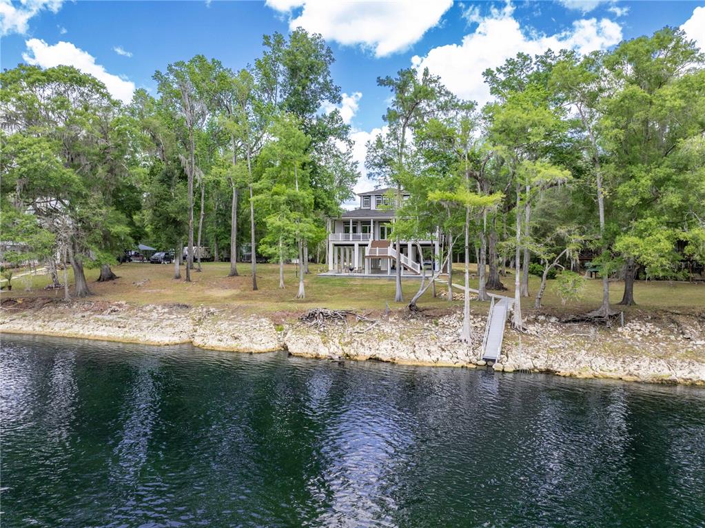 A multi-story house sits on a grassy bank overlooking a river with a wooden dock — 12890 NE 21ST TERRACE, BRANFORD, FL