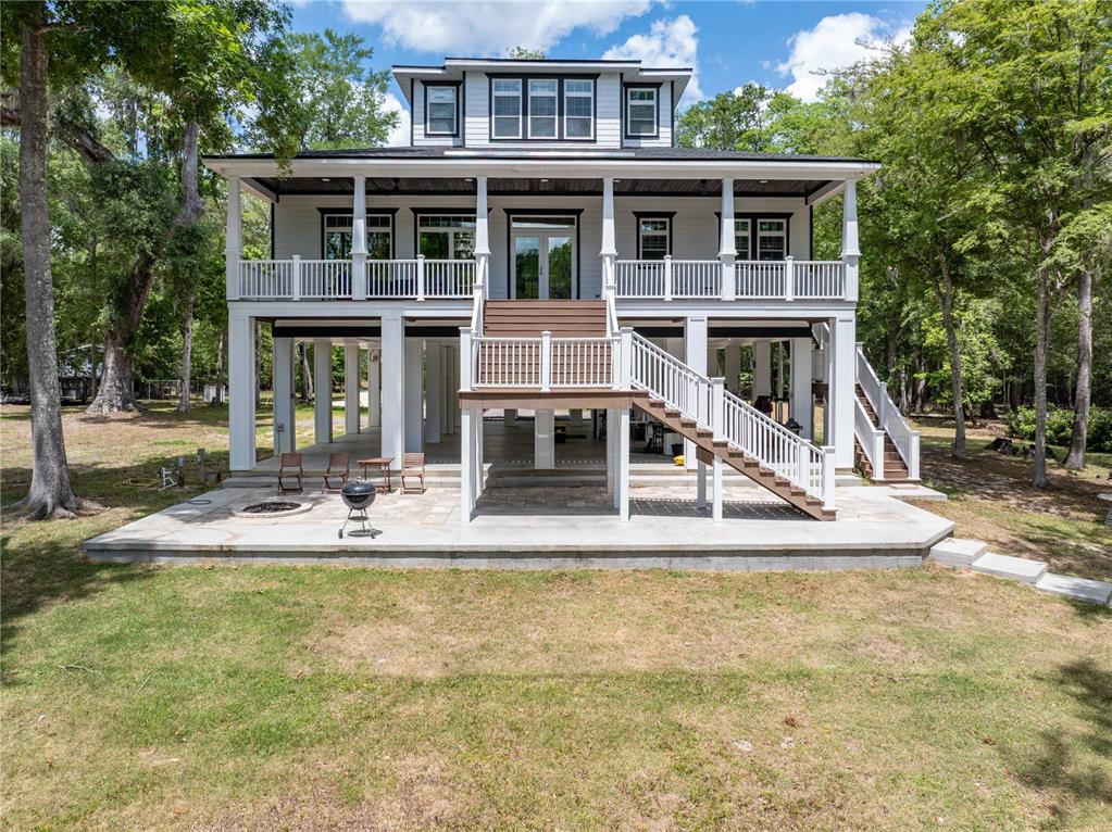 A three-story elevated house with a white exterior, wrap-around porch, and a ground-level patio — 12890 NE 21ST TERRACE, BRANFORD, FL