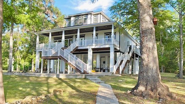 A white, multi-story house on stilts features a large wrap-around porch and outdoor stairs — 12890 NE 21ST TERRACE, BRANFORD, FL