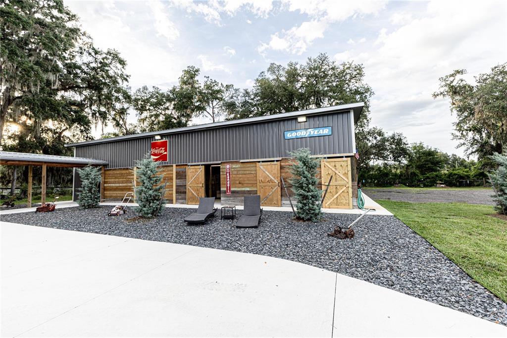 A metal-sided barn building features sliding wooden doors, lounge chairs, and vintage signage outdoors — 12523 CR 721, WEBSTER, FL