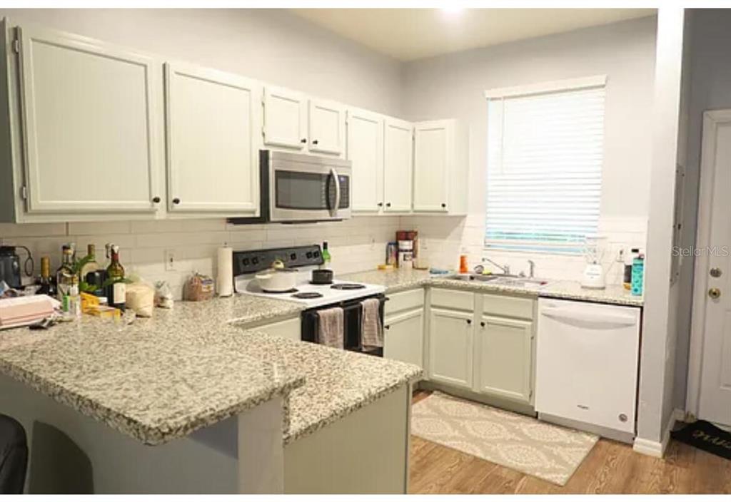 A kitchen with white cabinets, granite countertops, stainless steel appliances, and a light-colored backsplash — 4415 SW 34TH STREET UNIT 308, GAINESVILLE, FL