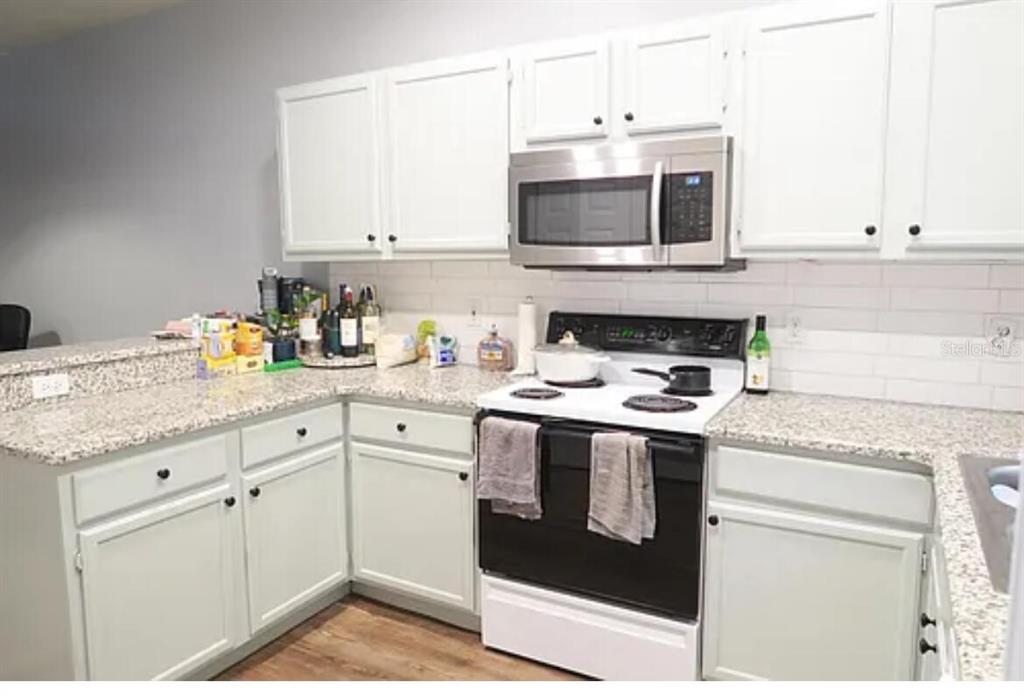 A kitchen features white cabinets, granite countertops, a subway tile backsplash, and stainless steel appliances — 4415 SW 34TH STREET UNIT 308, GAINESVILLE, FL