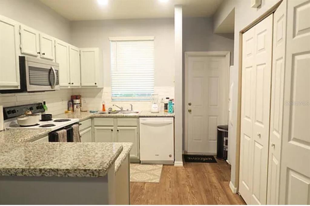 A kitchen features white cabinets, granite countertops, stainless steel appliances, and wood-look flooring — 4415 SW 34TH STREET UNIT 308, GAINESVILLE, FL