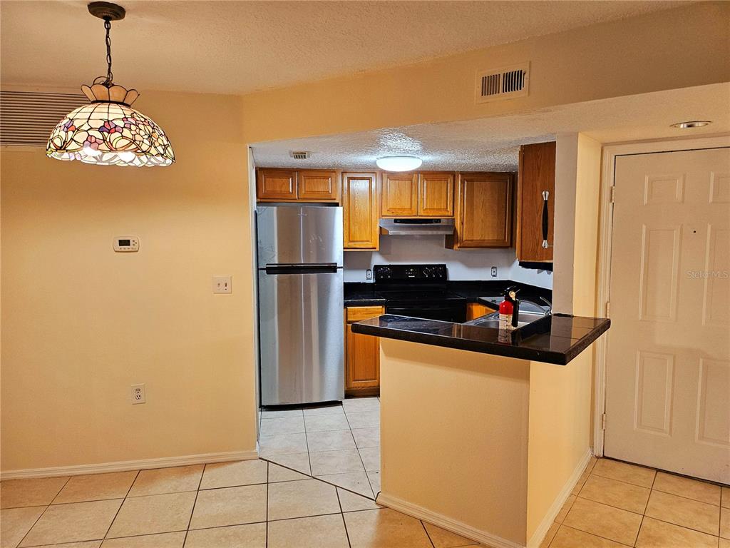 A kitchen with wood cabinets, stainless steel appliances, and a breakfast bar — 1916 LAKE ATRIUMS CIRCLE UNIT 25, ORLANDO, FL