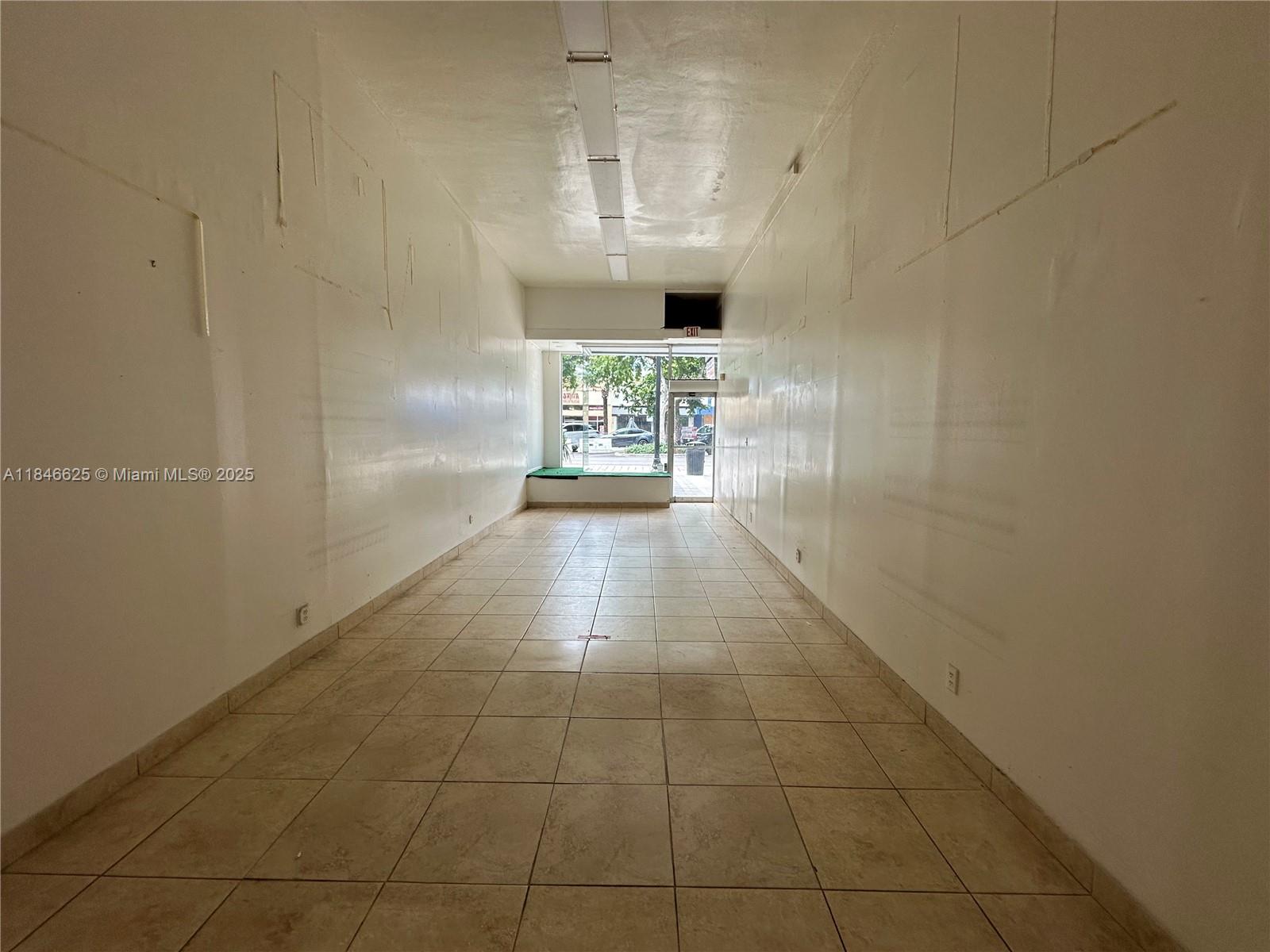 An empty, narrow commercial space features white walls, tiled floors, and a glass storefront entrance — 1932 Hollywood Blvd, Hollywood FL 33020, HOLLYWOOD, FL
