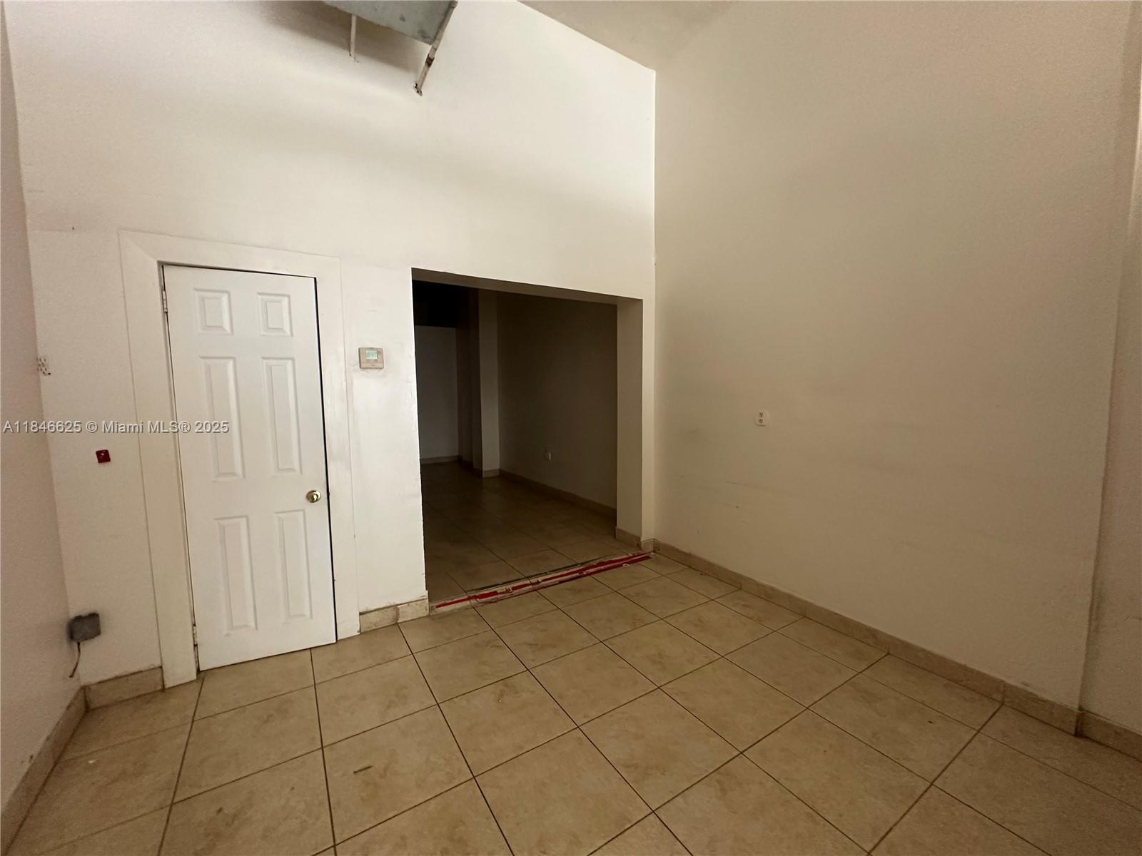 A room with beige tile flooring, a white door, and an open doorway to another area — 1932 Hollywood Blvd, Hollywood FL 33020, HOLLYWOOD, FL
