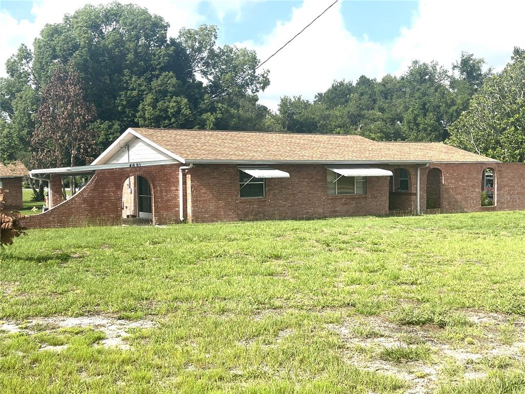 A single-story brick house with a gabled roof and arched entryway sits on a grassy lot — 4691 CR 118, WILDWOOD, FL