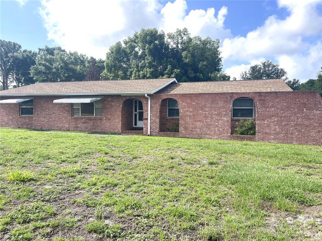 A single-story brick house features arched entryways and metal awnings over the windows — 4691 CR 118, WILDWOOD, FL