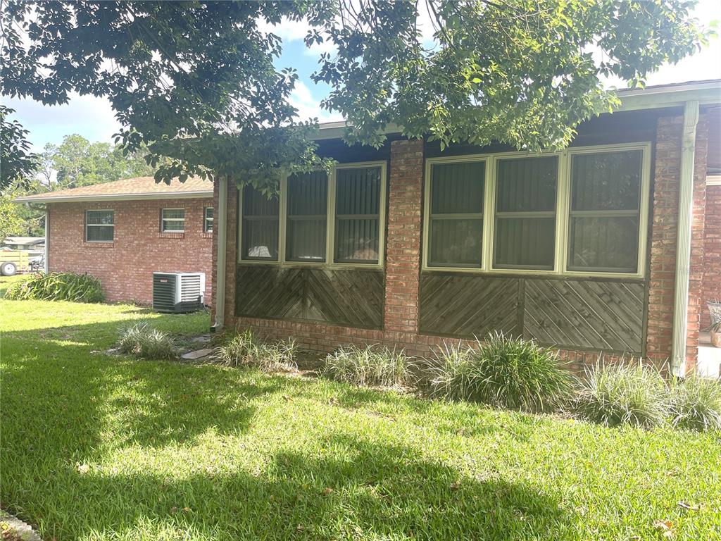A brick house exterior features large windows above diagonal wood paneling and a grassy lawn — 4691 CR 118, WILDWOOD, FL
