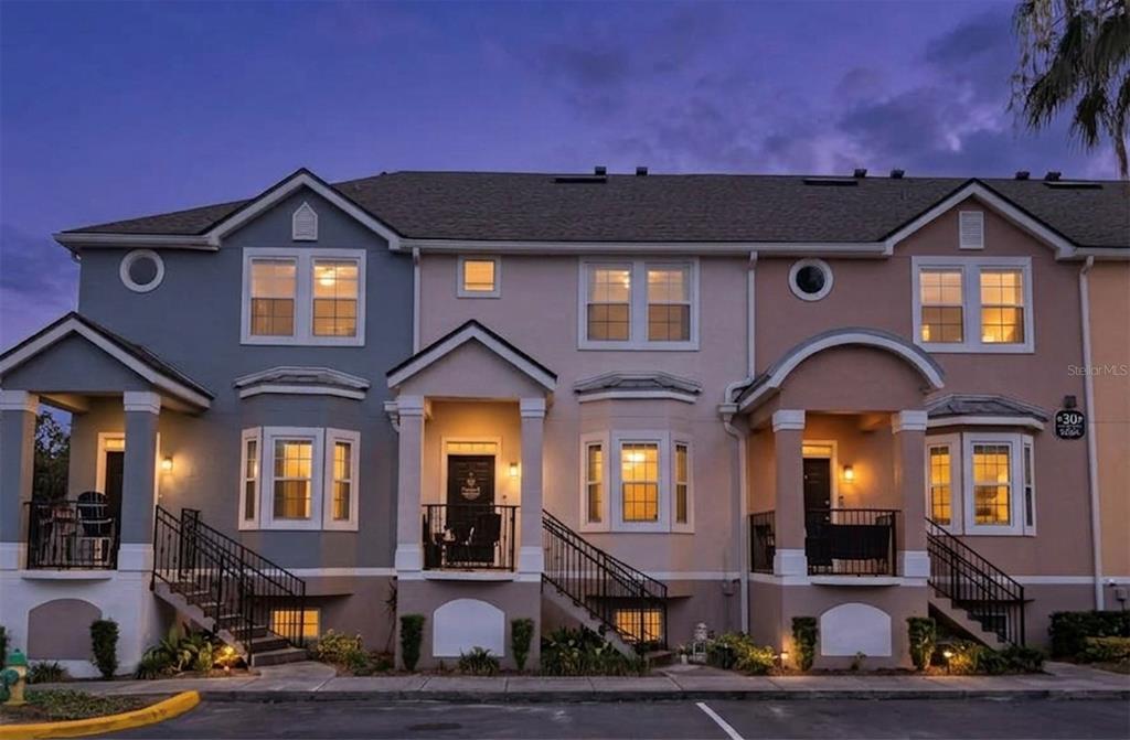 A three-story townhouse exterior with multiple porches, bay windows, and a paved parking area — 6624 TIME SQUARE AVENUE UNIT 104, ORLANDO, FL