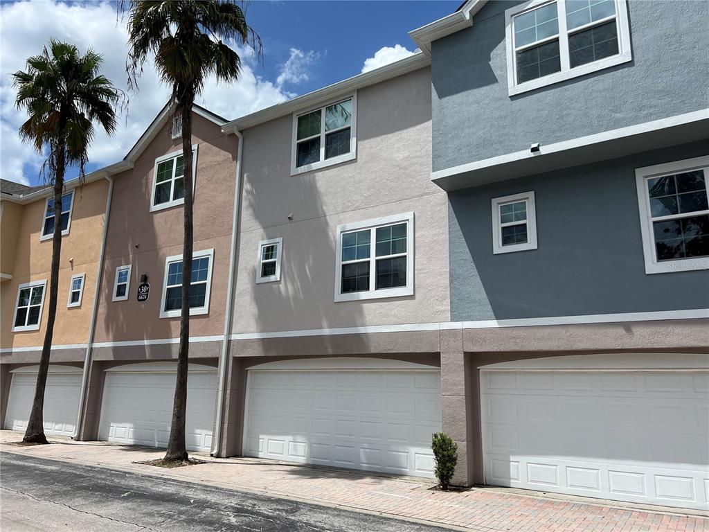 A row of multi-story townhomes features attached garages, stucco siding, and palm trees — 6624 TIME SQUARE AVENUE UNIT 104, ORLANDO, FL