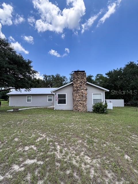 A single-story house with light siding and a prominent stone chimney stands on a lawn — 12601 DOUBLE RUN RD, ASTATULA, FL