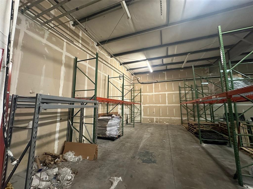 An industrial warehouse space features concrete floors, exposed ceiling beams, and metal storage racking units — 1630 TROPIC PARK DRIVE UNIT 1630, SANFORD, FL