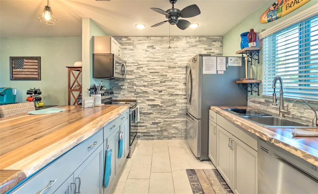 A kitchen features light blue cabinets, a wood countertop, and a stacked stone accent wall — 777 BEACH ROAD UNIT 1E, SARASOTA, FL