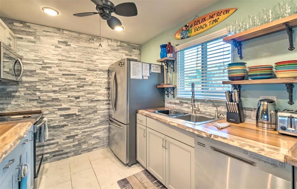 A kitchen features a stone-tiled accent wall, stainless steel appliances, and wooden countertops — 777 BEACH ROAD UNIT 1E, SARASOTA, FL