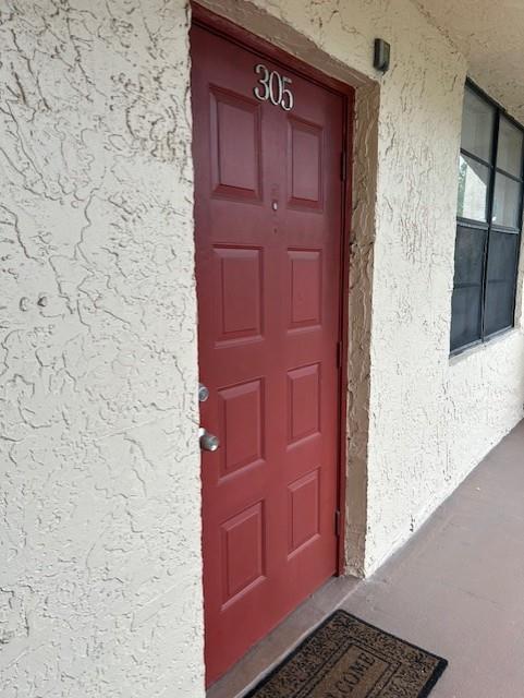 A red apartment door labeled 305 is set into a textured beige exterior wall — 3590 Blue Lake Drive # 305, Pompano Beach FL 33064, POMPANO BEACH, FL