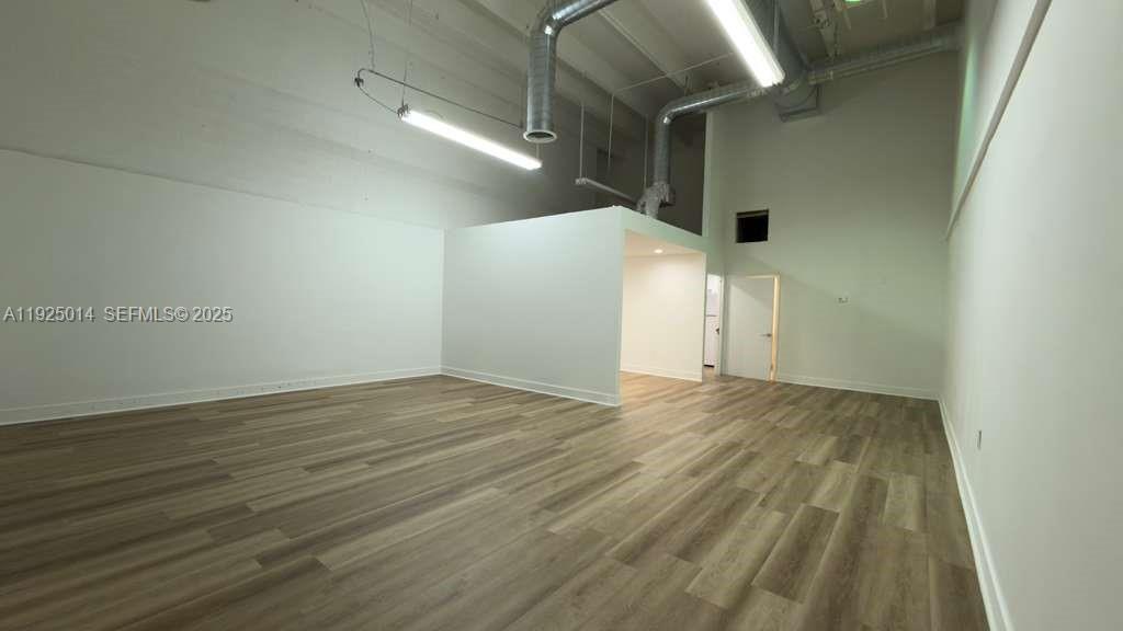 An empty room features high ceilings, exposed ductwork, pendant lighting, and wood-look flooring — 1671 W 37th St # 1, Hialeah FL 33012, HIALEAH, FL