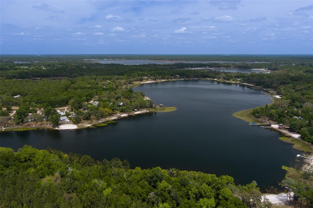 An aerial view shows a large lake surrounded by dense forest and residential properties — 8491 LILLY LAKE ROAD, MELROSE, FL