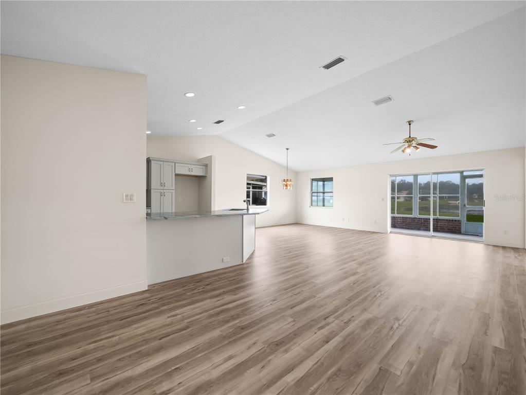 An open-concept living area features light wood-look flooring, a kitchen island, and sliding glass doors — 6341 SILVER LAKES DRIVE W, LAKELAND, FL
