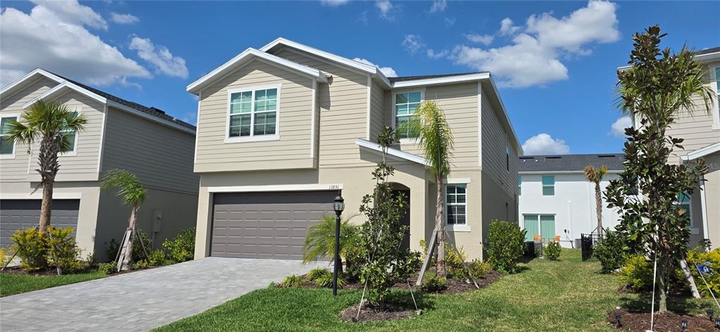 A two-story suburban house with beige siding, a gray garage door, and a paved driveway — 13851 LILAC SKY TERRACE UNIT NA, BRADENTON, FL