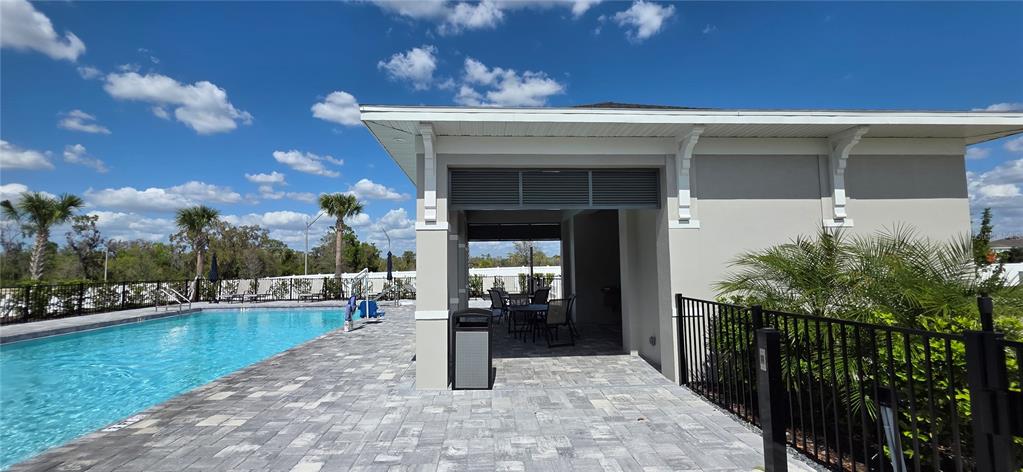 A swimming pool sits beside a covered patio area with outdoor seating and a trash receptacle — 13851 LILAC SKY TERRACE UNIT NA, BRADENTON, FL